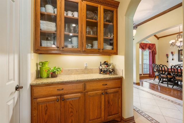bar featuring crown molding, arched walkways, a chandelier, and light tile patterned flooring