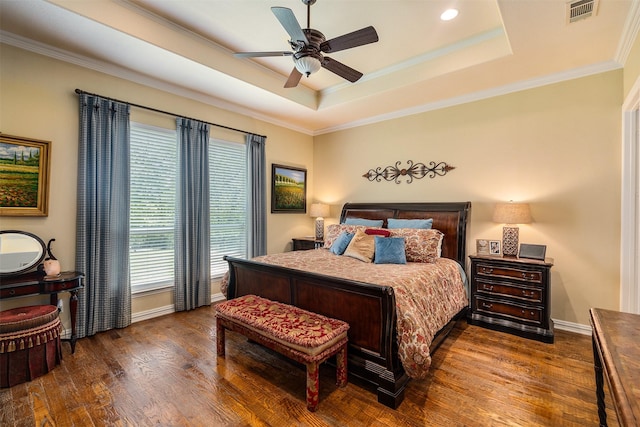 bedroom with a tray ceiling, wood finished floors, visible vents, ornamental molding, and baseboards