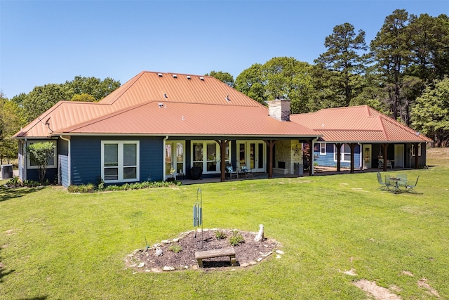 rear view of property with a lawn, central AC, a chimney, and metal roof