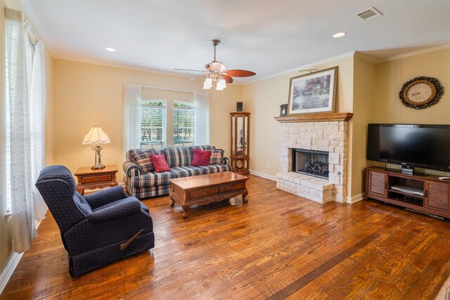 living area featuring wood finished floors, a stone fireplace, visible vents, and crown molding