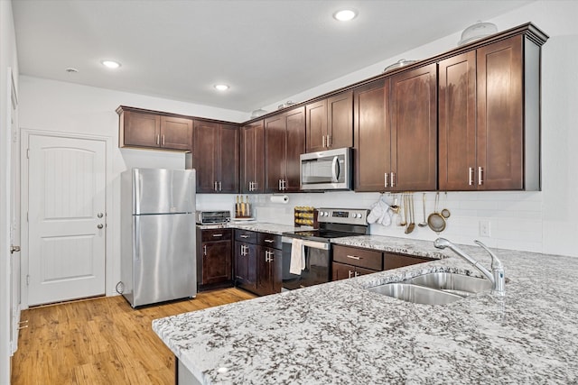 kitchen with light stone countertops, stainless steel appliances, a sink, and dark brown cabinets