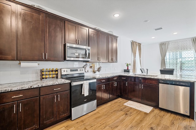 kitchen with light stone counters, stainless steel appliances, visible vents, a sink, and light wood-style flooring