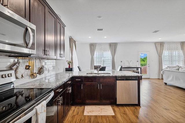 kitchen featuring stainless steel appliances, a sink, light wood-type flooring, light stone countertops, and a peninsula
