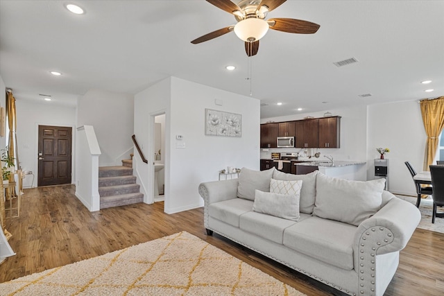 living room with light wood-style flooring, visible vents, recessed lighting, a ceiling fan, and stairs