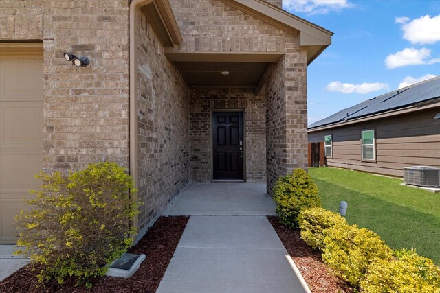 doorway to property with brick siding, a lawn, and central AC