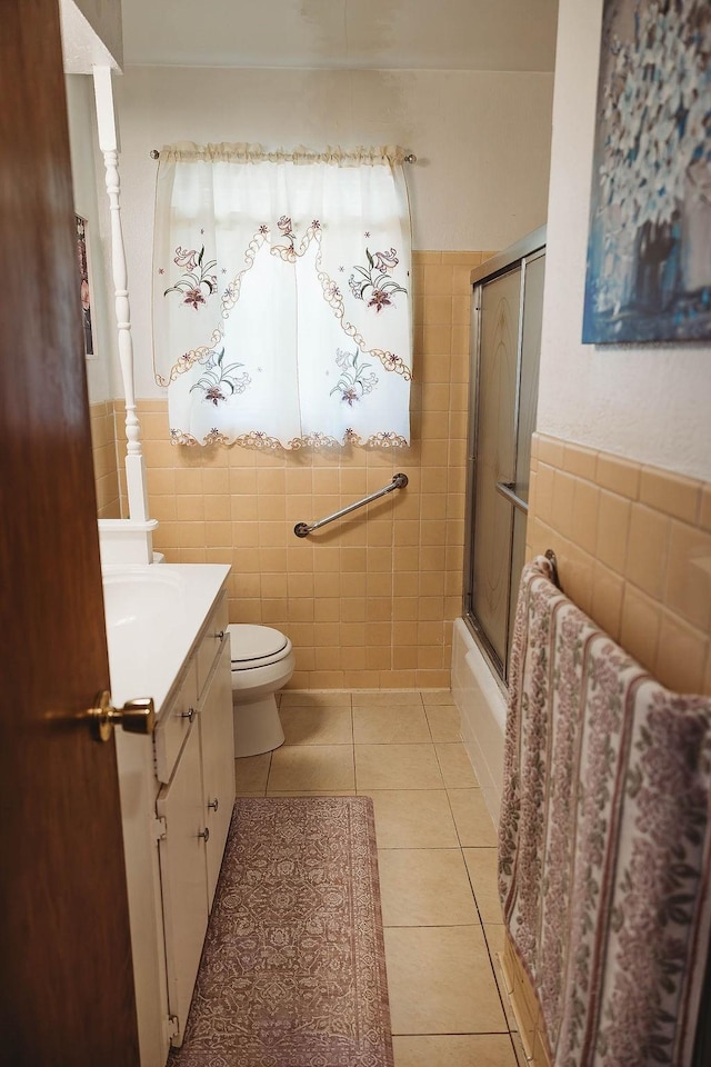 full bath featuring bath / shower combo with glass door, toilet, tile walls, tile patterned flooring, and vanity