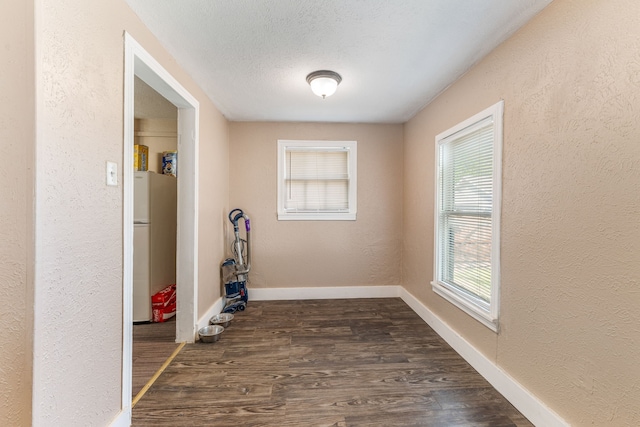 spare room with baseboards, a textured wall, a textured ceiling, and dark wood-style floors