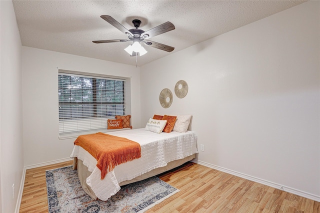 bedroom with light wood-style floors, a textured ceiling, baseboards, and a ceiling fan