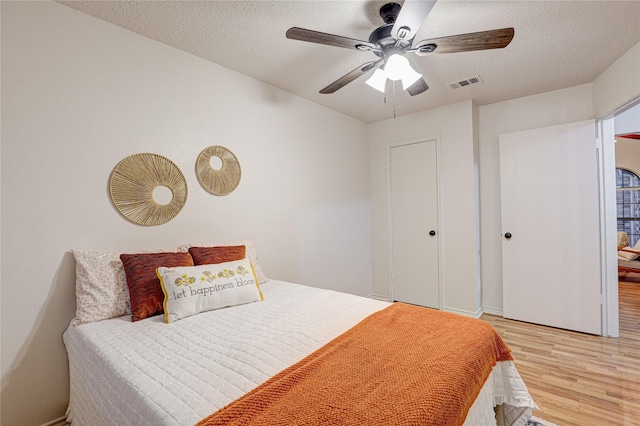 bedroom featuring visible vents, a textured ceiling, light wood-style floors, and a ceiling fan