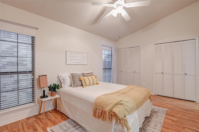 bedroom with a textured ceiling, light wood-style flooring, two closets, and vaulted ceiling