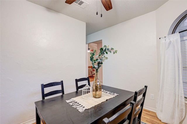dining space featuring ceiling fan, a textured ceiling, visible vents, light wood-style floors, and a textured wall