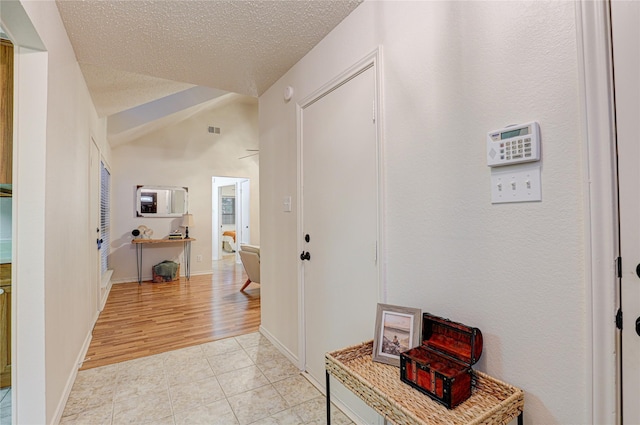 hall featuring light tile patterned floors, vaulted ceiling, a textured ceiling, and visible vents