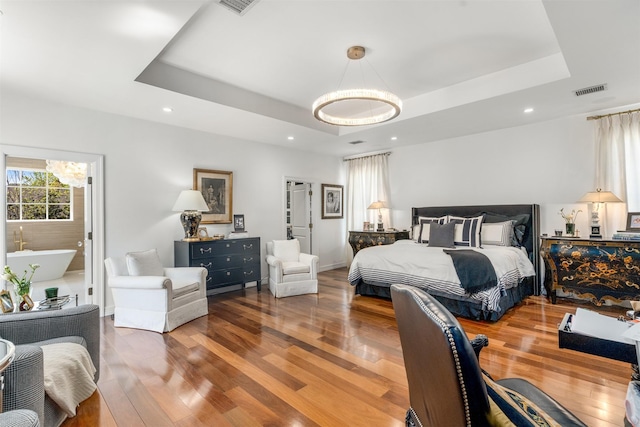 bedroom featuring wood finished floors, an inviting chandelier, recessed lighting, and a raised ceiling