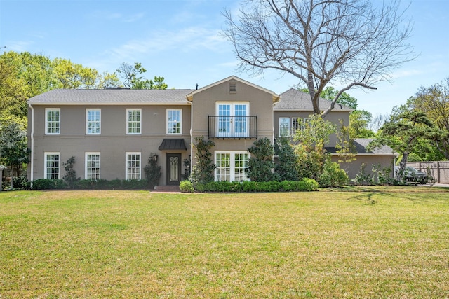 colonial inspired home with a balcony, a front yard, and stucco siding
