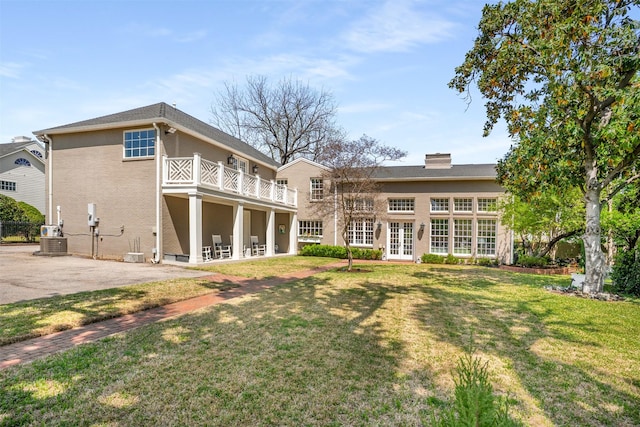 rear view of house featuring a patio area, a balcony, a chimney, french doors, and a yard