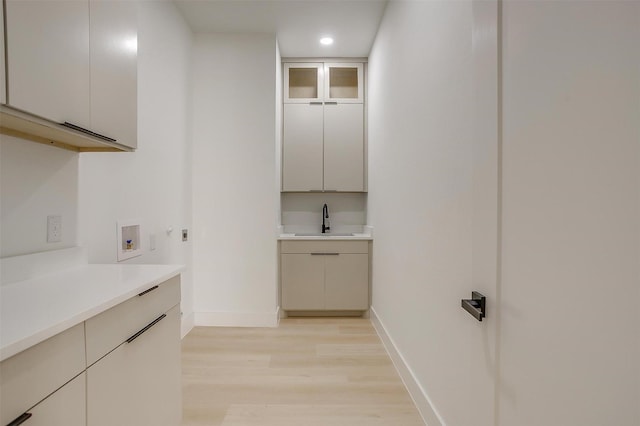 2229 Varsity Dr, Grand Prairie, TX 75051 - clothes washing area with a sink, light wood-style floors, baseboards, cabinet space, and washer hookup