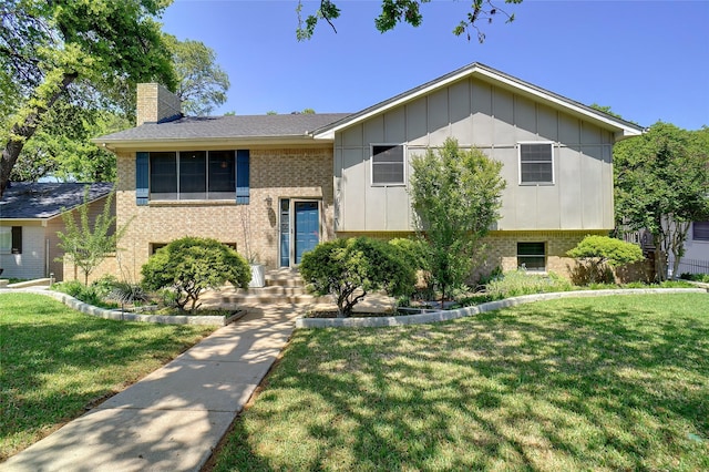 raised ranch with a chimney, brick siding, and a front yard