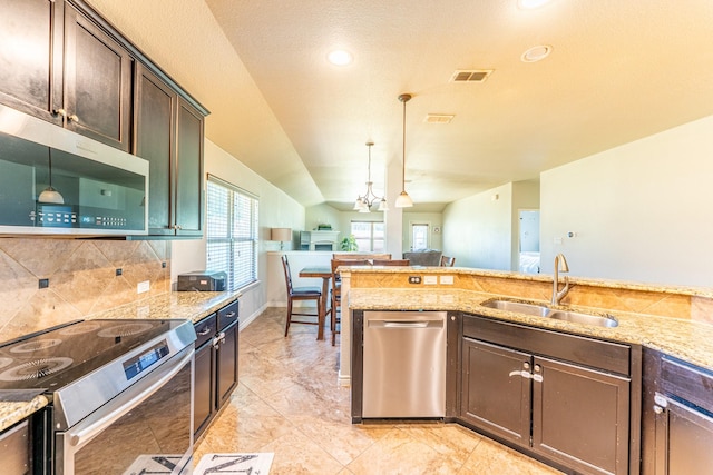 kitchen with light stone counters, stainless steel appliances, a sink, dark brown cabinetry, and hanging light fixtures