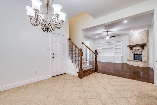 entryway featuring stairs, light tile patterned floors, baseboards, a large fireplace, and ceiling fan with notable chandelier