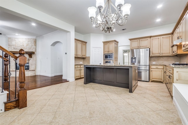 kitchen with under cabinet range hood, stainless steel appliances, backsplash, light tile patterned floors, and light stone countertops