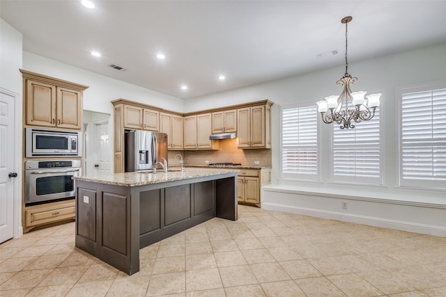 kitchen featuring stainless steel appliances, an inviting chandelier, light tile patterned floors, a center island with sink, and decorative backsplash