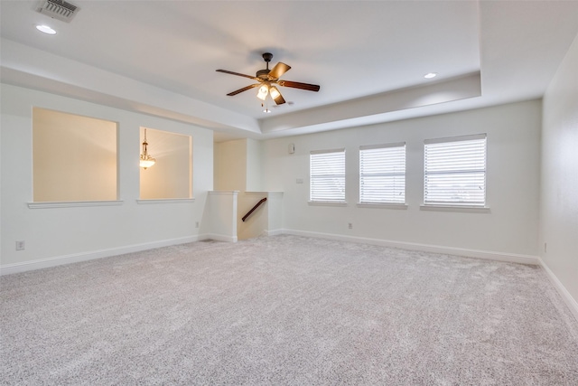 empty room featuring a raised ceiling, visible vents, a ceiling fan, carpet floors, and baseboards
