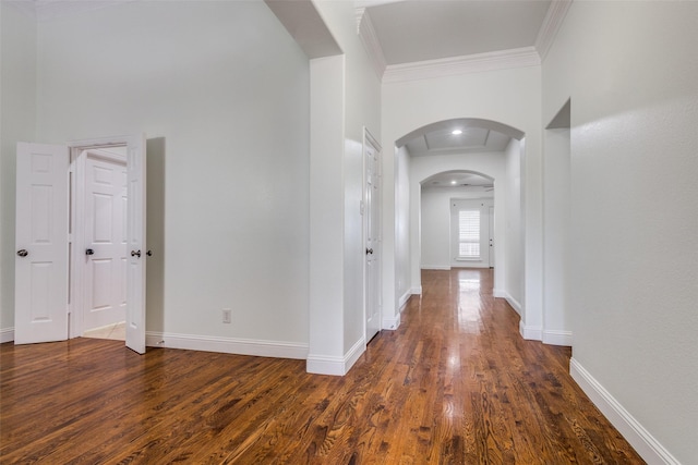 corridor featuring dark wood finished floors, arched walkways, ornamental molding, and baseboards
