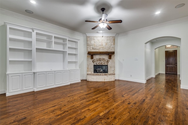 unfurnished living room with wood finished floors, a stone fireplace, a ceiling fan, ornamental molding, and arched walkways