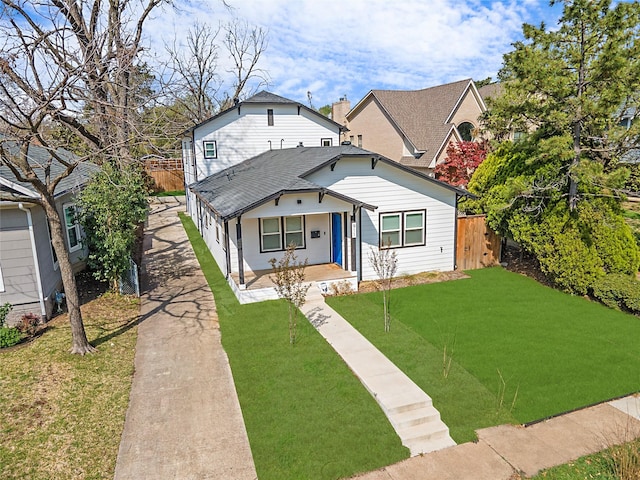 bungalow-style home with covered porch, roof with shingles, a front lawn, and fence