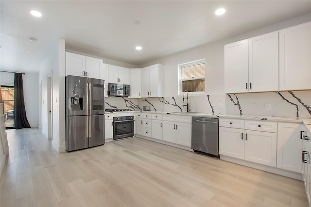 kitchen with backsplash, appliances with stainless steel finishes, white cabinetry, and a sink