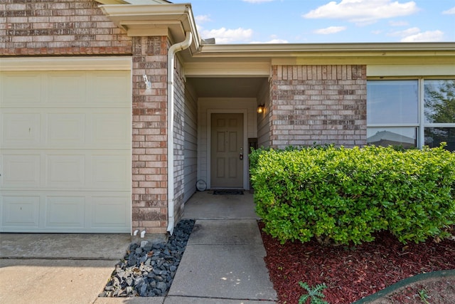 doorway to property with an attached garage and brick siding