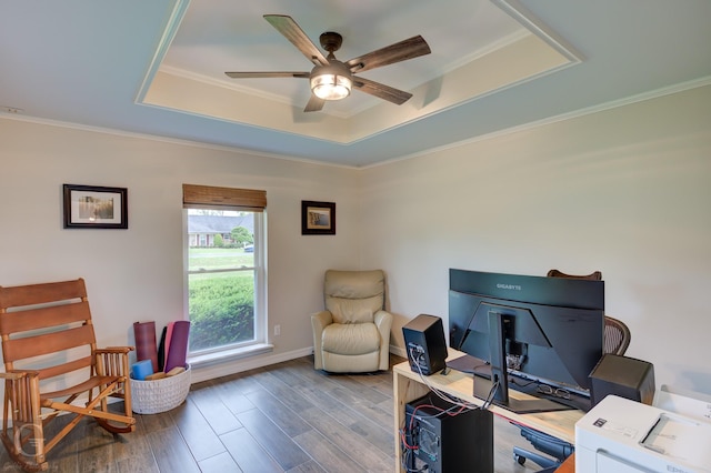 office area with a ceiling fan, wood finished floors, a raised ceiling, baseboards, and ornamental molding