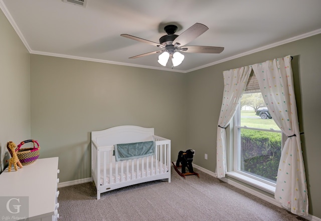 carpeted bedroom with ceiling fan, a nursery area, baseboards, and ornamental molding