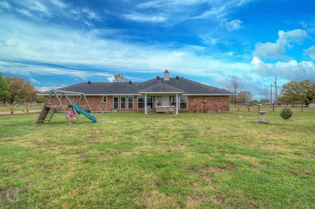 rear view of property with a lawn, a chimney, and a playground