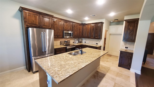kitchen featuring a sink, tasteful backsplash, dark brown cabinetry, light stone counters, and appliances with stainless steel finishes