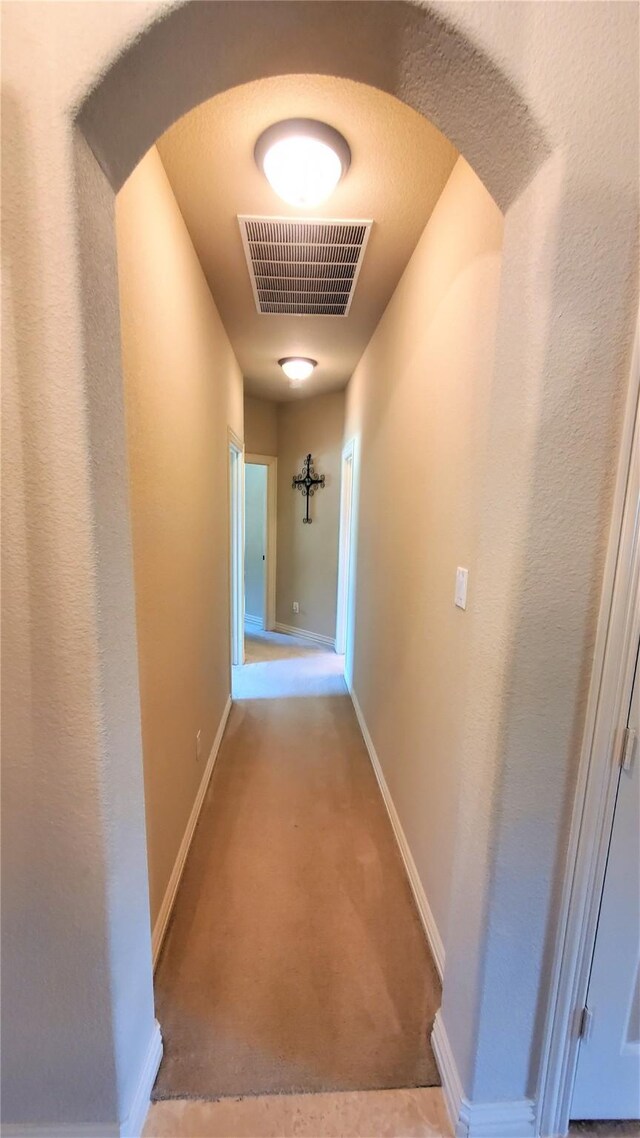 hallway with arched walkways, carpet floors, visible vents, and baseboards