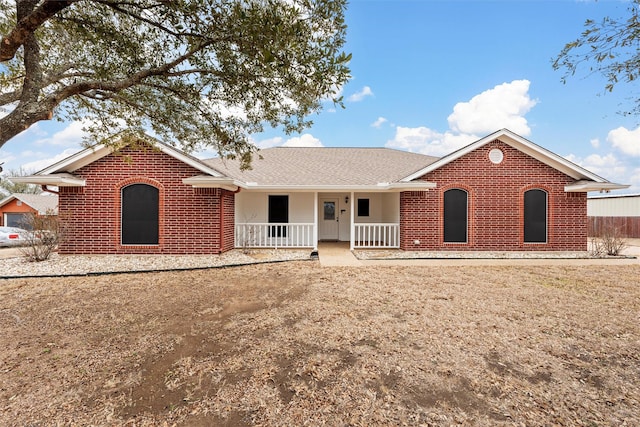 ranch-style house with brick siding, roof with shingles, and covered porch