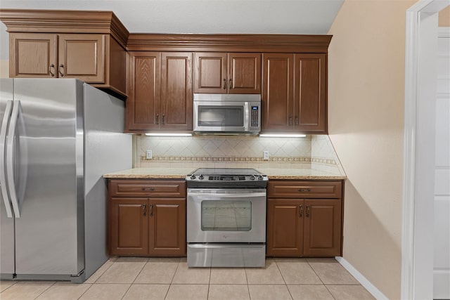 kitchen with light stone counters, light tile patterned floors, backsplash, baseboards, and appliances with stainless steel finishes