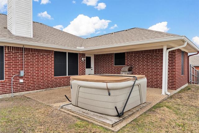 rear view of property with a chimney, brick siding, a hot tub, and roof with shingles