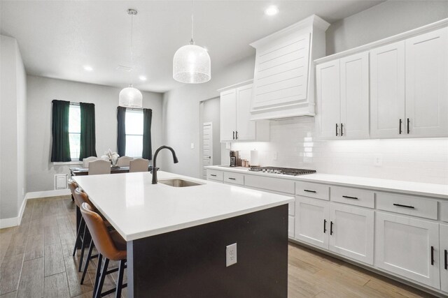 kitchen with decorative backsplash, light countertops, a sink, and an island with sink