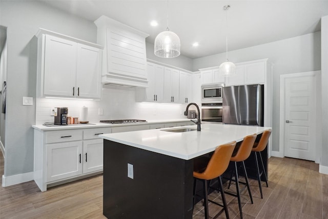 kitchen with light wood-style flooring, a sink, backsplash, light countertops, and appliances with stainless steel finishes