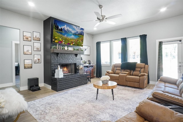 living area featuring wood finished floors, a brick fireplace, ceiling fan, and plenty of natural light
