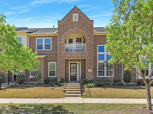 view of property with brick siding, a balcony, a shingled roof, and a front yard