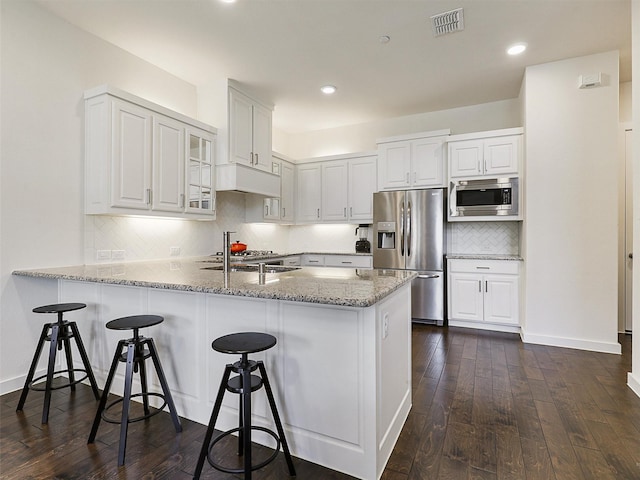 kitchen featuring stainless steel appliances, a peninsula, visible vents, white cabinetry, and decorative backsplash