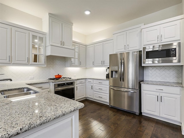 kitchen with a sink, glass insert cabinets, light stone countertops, tasteful backsplash, and appliances with stainless steel finishes