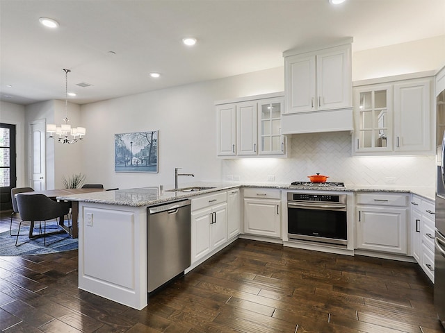 kitchen featuring a peninsula, a sink, dark wood-style flooring, a notable chandelier, and appliances with stainless steel finishes