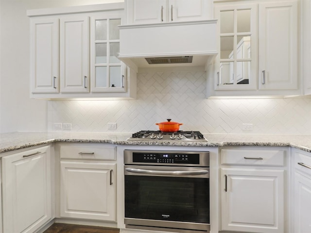 kitchen with white cabinets, stainless steel appliances, custom exhaust hood, and decorative backsplash