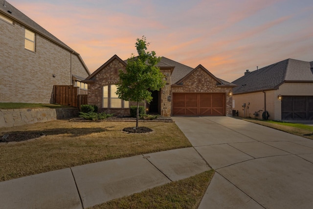 french country inspired facade with a front lawn, driveway, brick siding, and a garage