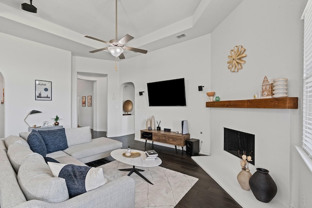 living area with a ceiling fan, wood finished floors, arched walkways, and a fireplace with raised hearth