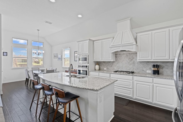kitchen with custom exhaust hood, a sink, lofted ceiling, appliances with stainless steel finishes, and dark wood-style floors